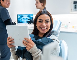 Patient smiling while holding mirror in treatment chair