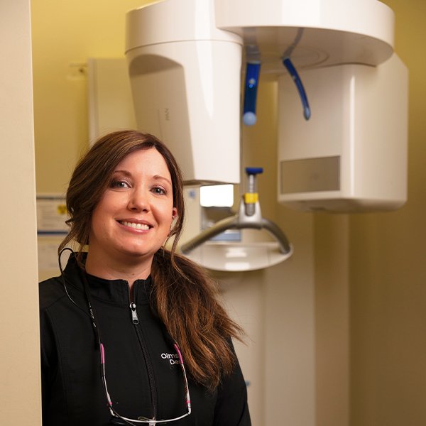 Dental team member smiling next to the 3 D C T cone beam imaging scanner