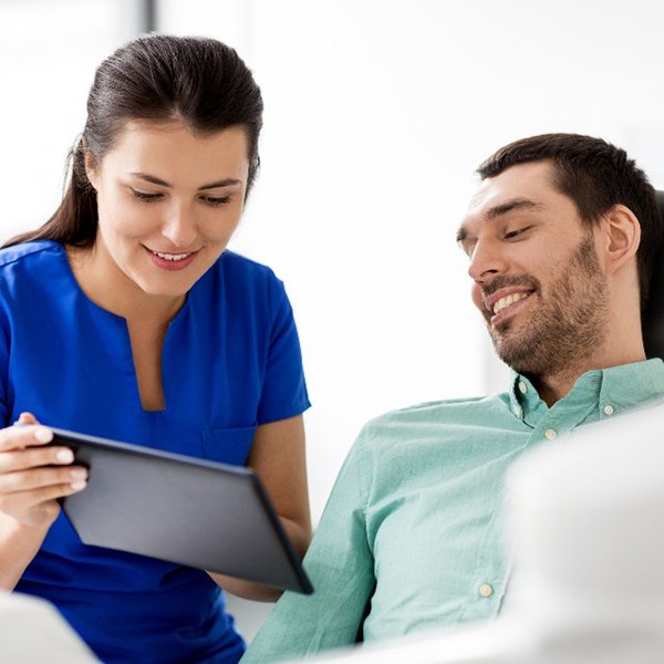 Dental assistant and patient smiling while looking at tablet
