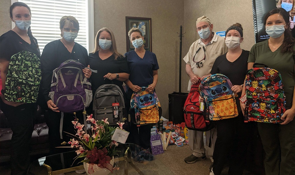 Team members holding backpacks filled with food for the stuff the bus food drive