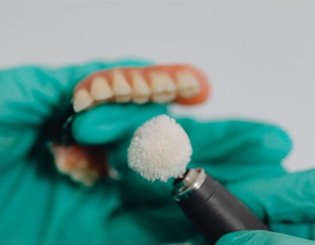 Gloved hands polishing partial denture
