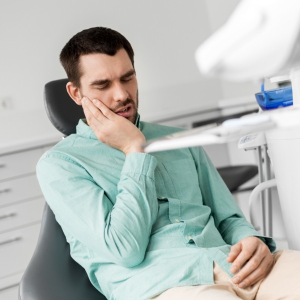 Man in need of emergency dentistry holding his cheek in pain