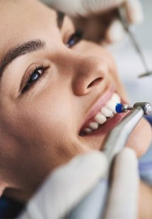 Woman in dental chair smiling as teeth are professionally polished