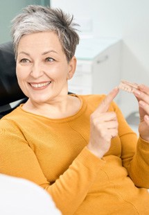 Woman in yellow shirt in dental chair holding dentures