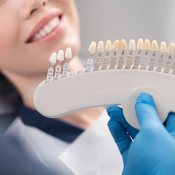 Dentist holding shade scale up to smiling patient's teeth