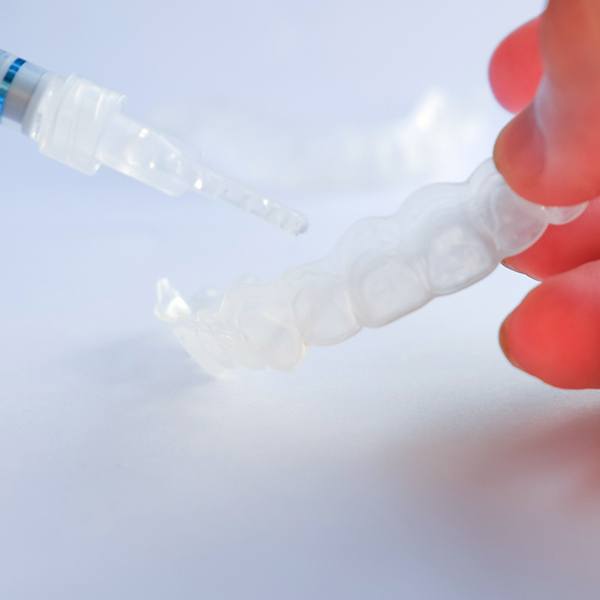 Hand holding a custom-fitted tray and whitening gel